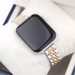 Bracelet Apple Watch EzStrap en métal inoxydable au design lisse et raffiné, style luxe avec maillons bicolores argent et or, présenté sur un coussin blanc dans un coffret.