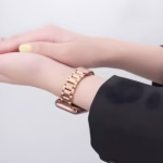 Bracelet Apple Watch EzStrap en métal rose doré à maillons classiques, au style élégant et à finition lisse, porté au poignet d’une femme en veste noire.