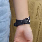 Bracelet Apple Watch EzStrap en cuir lisse noir, style élégant à enroulement double, porté au poignet d’une personne en jean devant un fond imprimé de texte.