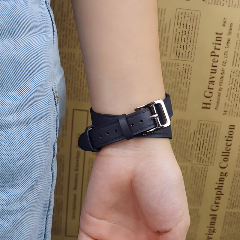 Bracelet Apple Watch EzStrap en cuir lisse noir, style élégant à enroulement double, porté au poignet d’une personne en jean devant un fond imprimé de texte.
