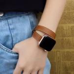 Bracelet Apple Watch EzStrap en cuir lisse marron, style élégant à enroulement double, porté au poignet d’une femme posant la main dans une poche de jean.