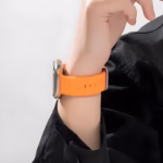 Bracelet Apple Watch EzStrap en silicone orange de style sport, avec un design ondulé, porté au poignet d’une personne habillée en noir.
