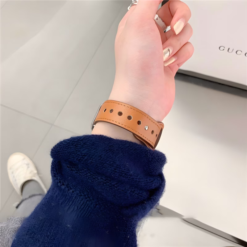 Bracelet Apple Watch EzStrap en cuir lisse couleur camel avec couture apparente, style élégant, porté au poignet d’une femme dans un environnement moderne.