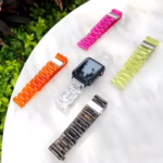 Bracelet Apple Watch EzStrap en plastique lisse transparent, de style élégant à maillons articulés, présenté avec d'autres coloris sur une table en marbre en extérieur.