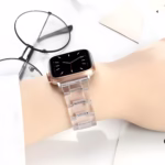 Bracelet Apple Watch EzStrap en plastique transparent à maillons articulés, au design élégant et lisse, porté au poignet d’une personne posée sur un bureau.