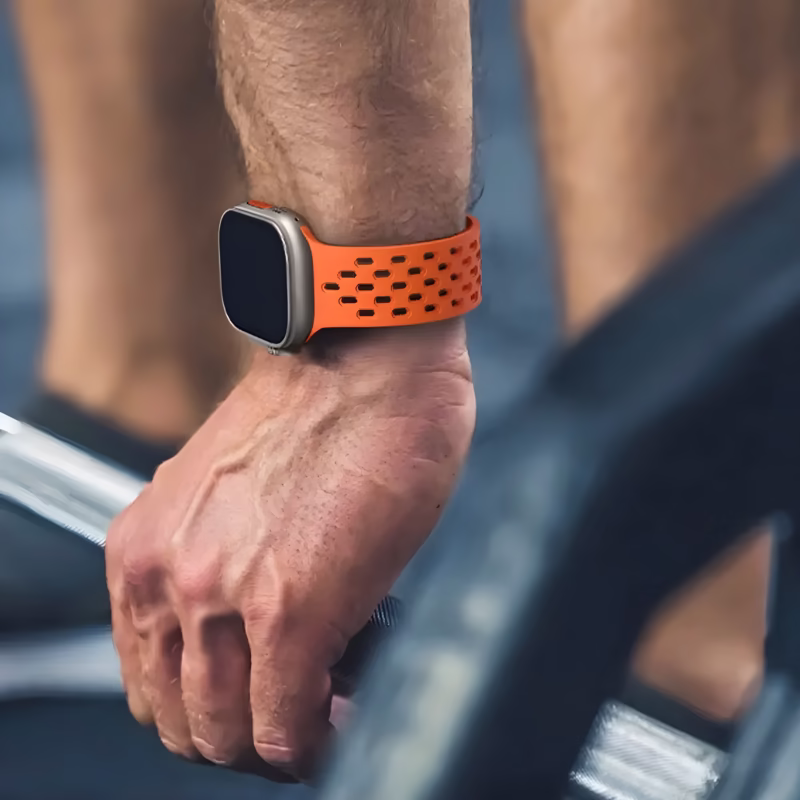 Bracelet Apple Watch EzStrap en silicone orange perforé, style sport, porté au poignet d’un homme tenant une barre de musculation.
