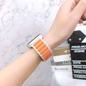 Bracelet Apple Watch EzStrap en silicone perforé texturé, style sport, avec inserts orange, porté au poignet d’une femme devant un mur en marbre.