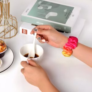 Bracelet Apple Watch EzStrap en textile élastique style chouchou, aux tons dégradés rose, orange et jaune, porté au poignet d'une femme prenant un café à une table blanche.