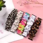 Bracelet Apple Watch EzStrap en textile élastique style chouchou, au design texturé et motifs variés comme léopard, floral et dégradé, présenté à plat sur un fond rose avec des éléments décoratifs.