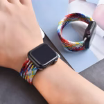 Bracelet Apple Watch EzStrap en nylon tressé multicolore, style sport avec finition texturée, porté au poignet d’une personne et posé à côté sur une surface sombre.