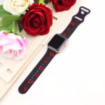 Bracelet Apple Watch EzStrap en silicone élégant bicolore, avec motif floral gravé rouge sur fond noir, posé à plat à côté de roses artificielles.