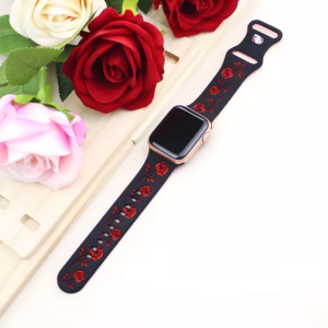 Bracelet Apple Watch EzStrap en silicone élégant bicolore, avec motif floral gravé rouge sur fond noir, posé à plat à côté de roses artificielles.