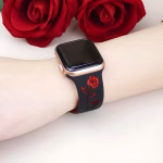 Bracelet Apple Watch EzStrap en silicone élégant, bicolore noir et rouge, avec motif floral gravé, porté au poignet d’une personne devant des roses rouges.