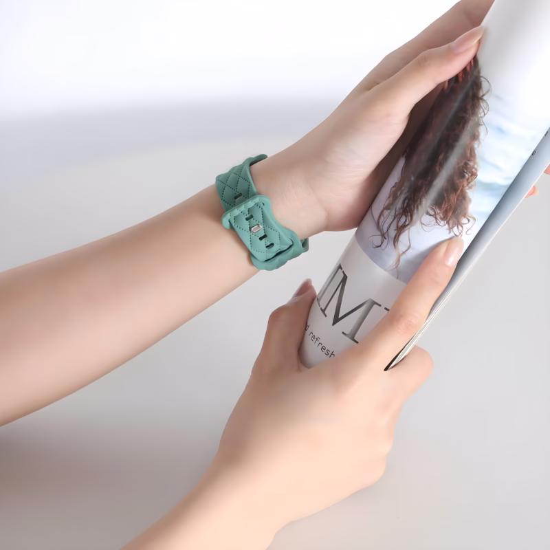 Bracelet Apple Watch EzStrap en silicone vert au design matelassé, style élégant, porté au poignet d’une femme lisant un magazine.