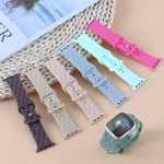 Bracelets Apple Watch EzStrap en silicone matelassé de style élégant, déclinés en plusieurs coloris pastel, posés à plat sur une surface beige avec l’un des bracelets monté sur une montre connectée.