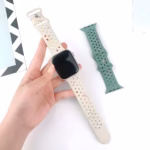 Bracelet Apple Watch EzStrap en silicone perforé de style sport, blanc transparent avec éclats multicolores, tenu en main sur fond blanc à côté d’un second bracelet vert.