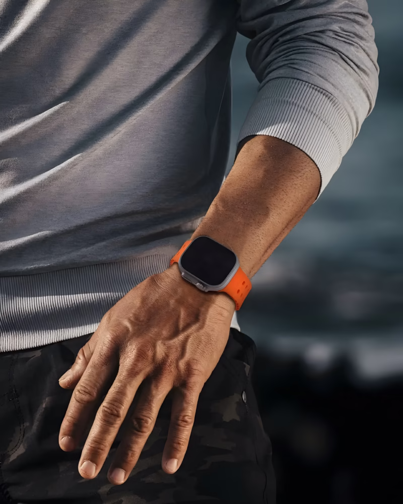 Bracelet Apple Watch EzStrap en silicone orange perforé, style sport, porté au poignet d’un homme en extérieur près de la mer.