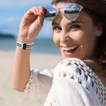 Bracelet Apple Watch EzStrap en silicone perforé blanc et noir, au style sport, porté au poignet d’une femme souriante sur une plage ensoleillée.