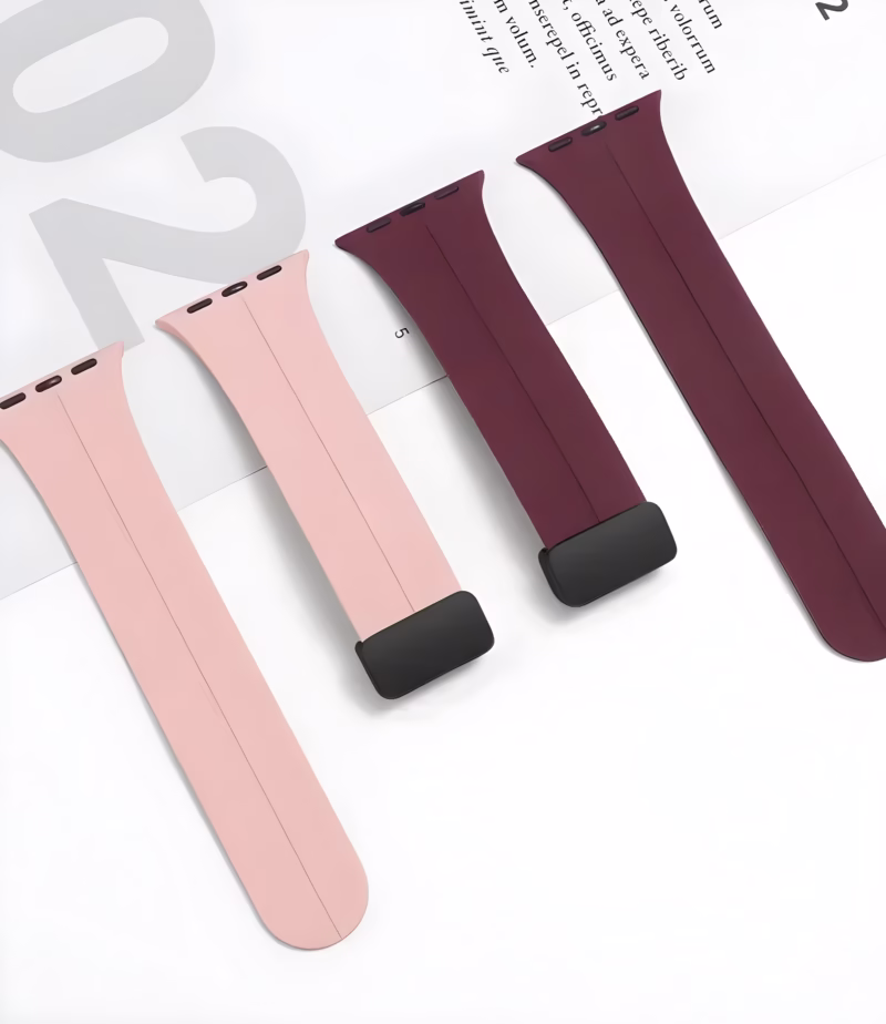 Bracelet Apple Watch EzStrap en silicone lisse, de style sport, présenté en deux coloris rose pâle et bordeaux, posé à plat sur une feuille blanche de magazine.