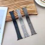 Bracelet Apple Watch EzStrap en acier inoxydable à construction articulée, finition lisse et style premium, présenté en trois coloris posés sur une surface beige près d’un plateau en bois ondulé.