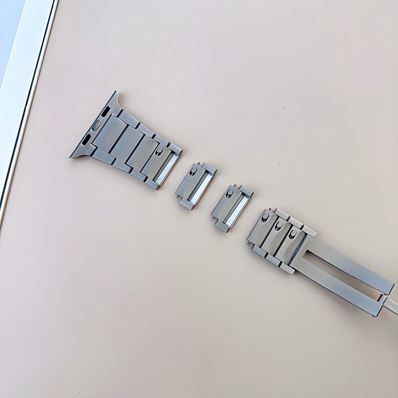 Bracelet Apple Watch EzStrap en métal inoxydable à construction articulée, style luxe avec finition lisse, posé en pièces détachées sur une surface beige.