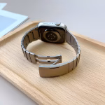 Bracelet Apple Watch EzStrap en acier inoxydable à construction articulée, finition lisse de style premium, présenté en gros plan sur un plateau en bois clair.