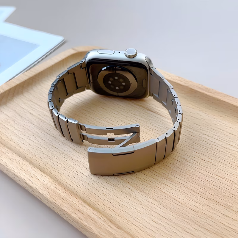 Bracelet Apple Watch EzStrap en acier inoxydable à construction articulée, finition lisse de style premium, présenté en gros plan sur un plateau en bois clair.
