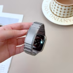 Bracelet Apple Watch EzStrap en métal inoxydable, style luxe avec finitions lisses, tenu en main devant une tasse et un magazine sur une table.