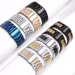 Bracelet Apple Watch EzStrap en acier inoxydable finition brossée à maillons métalliques, de style luxe, présenté en plusieurs coloris sur des supports cylindriques blancs.
