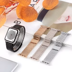 Bracelet Apple Watch EzStrap en acier inoxydable à maille articulée lisse, style luxe, présenté en quatre coloris métalliques posés sur un magazine de mode avec des feuilles décoratives en arrière-plan.