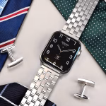 Bracelet Apple Watch EzStrap en acier inoxydable à maillons biseautés, finition brossée et lisse, de style luxe, posé sur un fond élégant avec cravates et boutons de manchette.