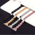 Bracelet Apple Watch EzStrap en métal brillant, style élégant à maillons chevrons, décliné en plusieurs coloris et présenté à plat sur un livre posé sur une surface noire.
