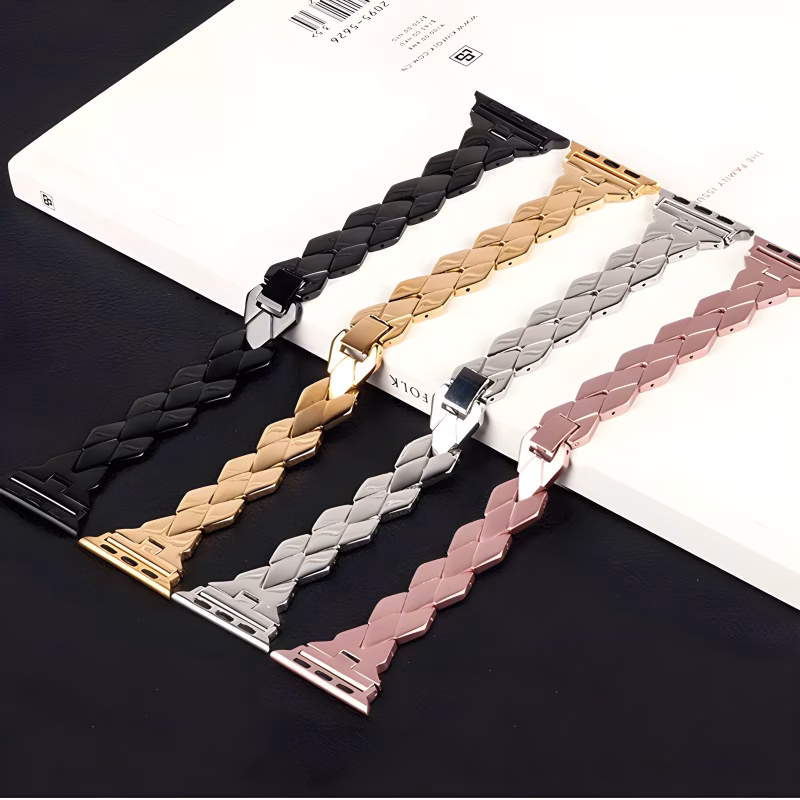 Bracelet Apple Watch EzStrap en métal brillant, style élégant à maillons chevrons, décliné en plusieurs coloris et présenté à plat sur un livre posé sur une surface noire.