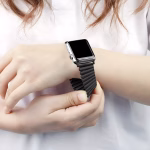 Bracelet Apple Watch EzStrap en métal brossé noir, de style élégant avec maillons flexibles extensibles, porté au poignet d’une femme en train de l’ajuster.