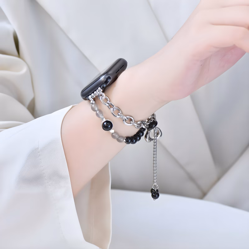 Bracelet Apple Watch EzStrap en métal élégant orné de perles brillantes noires et grises, porté au poignet d’une femme vêtue d’un haut en satin clair.