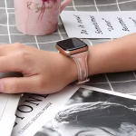 Bracelet Apple Watch EzStrap en cuir lisse imprimé à finition scintillante, de style élégant, porté au poignet d’une femme, posé sur une table avec une tasse rose et un magazine.