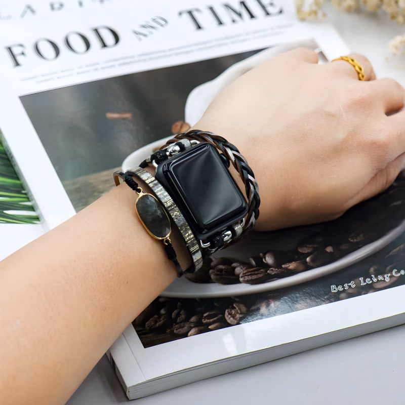 Bracelet Apple Watch EzStrap en cuir multibrins avec ornements métalliques brillants, style élégant et artisanal, porté au poignet d’une personne lisant un magazine.