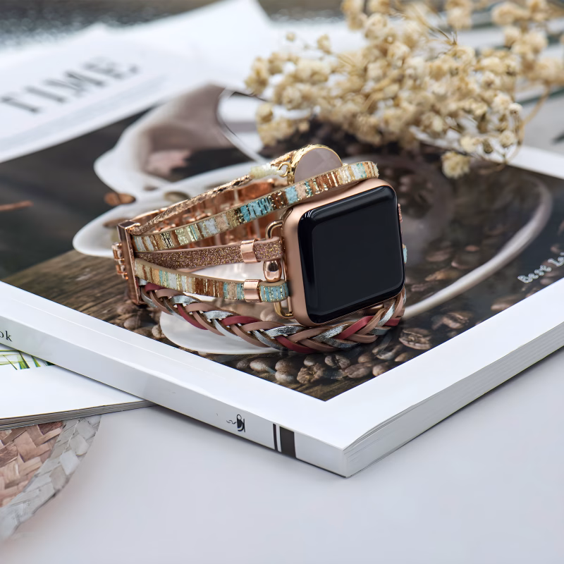 Bracelet Apple Watch EzStrap en cuir multibrins orné de détails métalliques scintillants, au style élégant et artisanal, posé sur un magazine décoratif avec des fleurs séchées en arrière-plan.