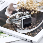 Bracelet Apple Watch EzStrap en cuir multibrins avec ornements métalliques scintillants, de style artisanal et élégant, posé en gros plan sur un magazine décoratif avec fleurs séchées.