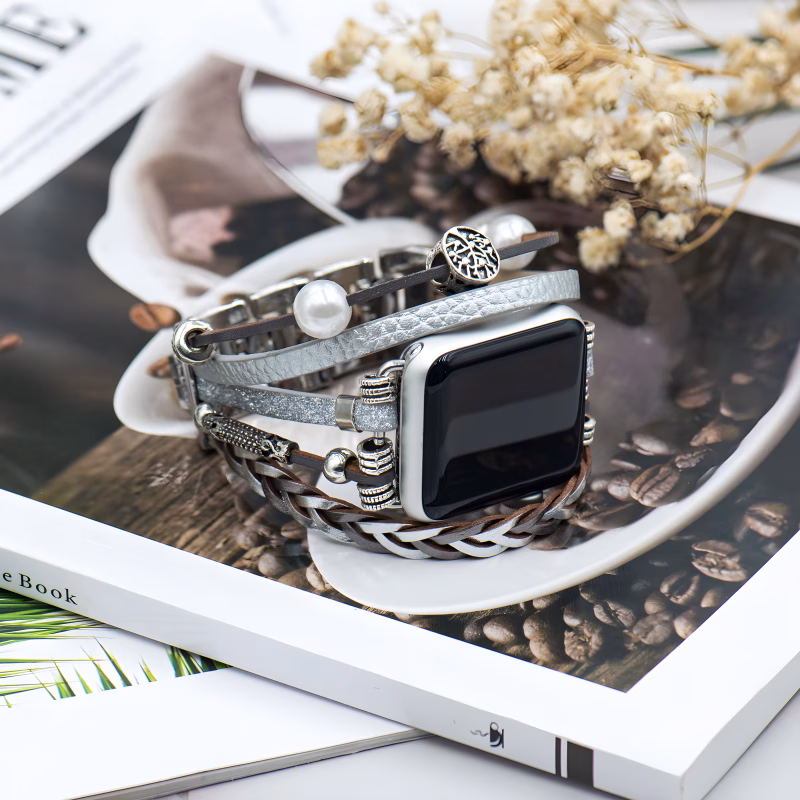 Bracelet Apple Watch EzStrap en cuir multibrins avec ornements métalliques scintillants, de style artisanal et élégant, posé en gros plan sur un magazine décoratif avec fleurs séchées.