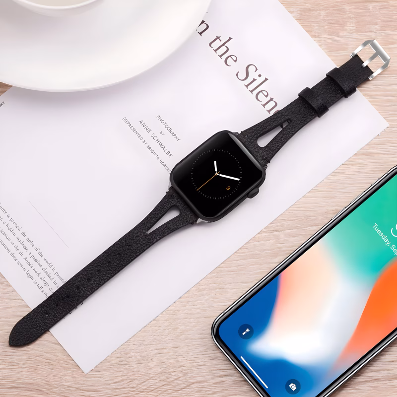 Bracelet Apple Watch EzStrap en cuir lisse noir avec fente ornementale, style élégant, posé sur une feuille imprimée près d’un smartphone et d’une tasse.