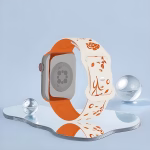 Bracelet Apple Watch EzStrap en silicone gravé au design floral et oiseau stylisé, présenté en gros plan sur un miroir avec fond bleu clair.