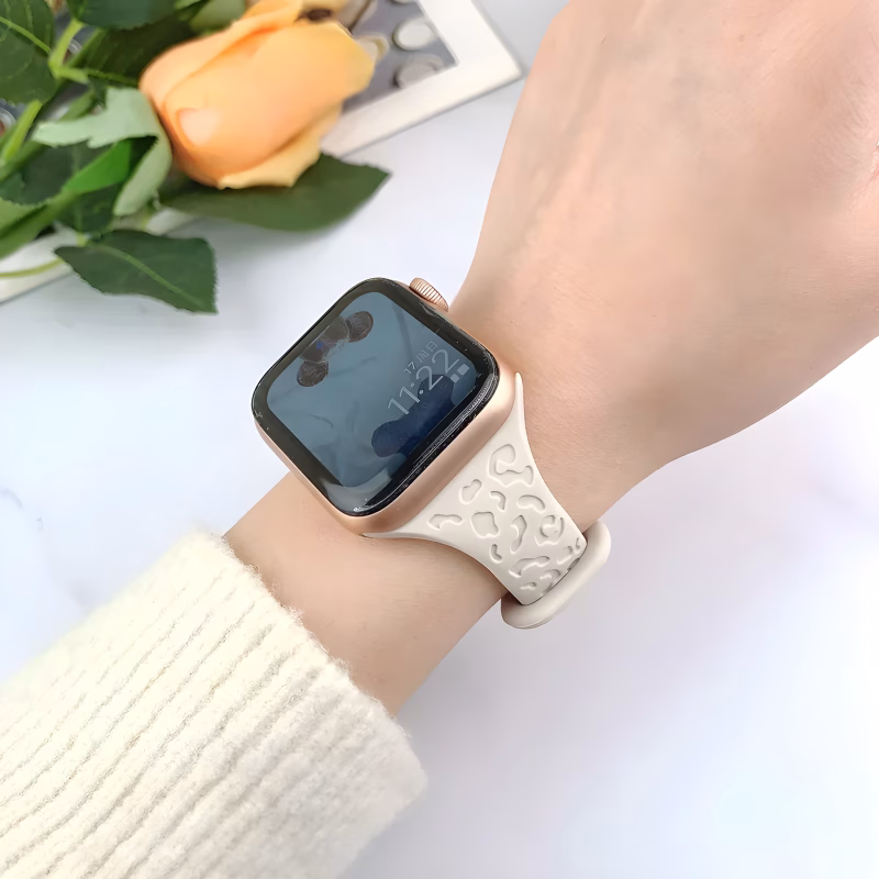 Bracelet Apple Watch EzStrap en silicone texturé de couleur crème, style sport, avec un motif léopard en relief, porté au poignet d’une personne vêtue d’un pull blanc.