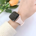 Bracelet Apple Watch EzStrap en silicone rose clair, style sport avec motif léopard en relief, porté au poignet d'une femme sur fond floral.