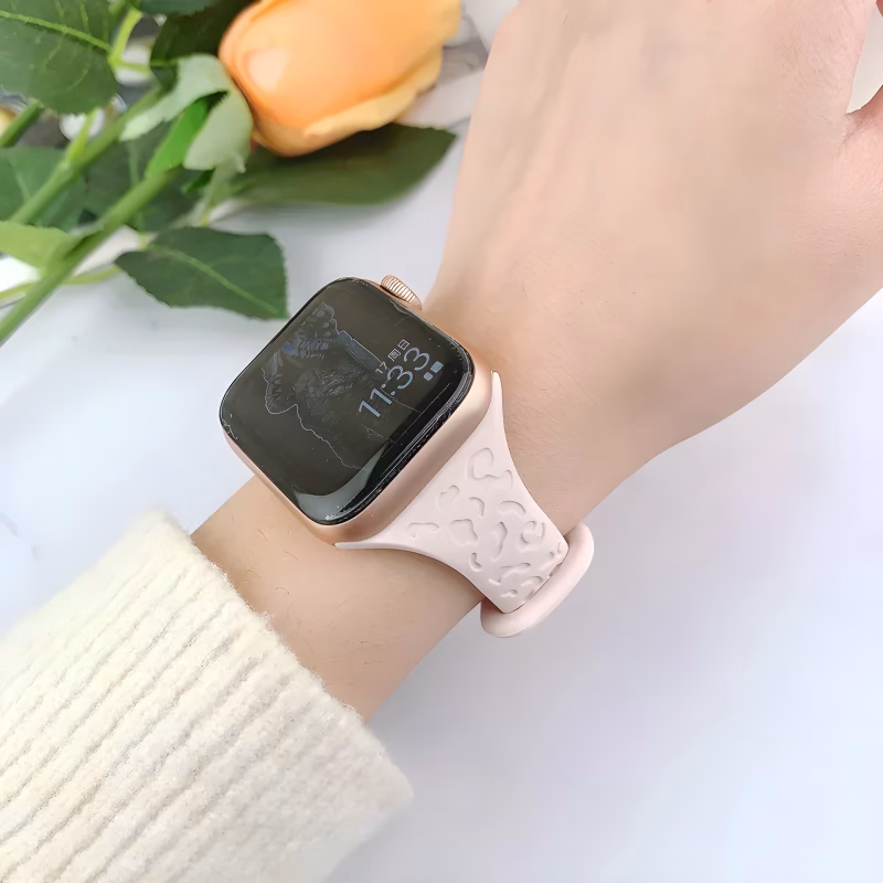 Bracelet Apple Watch EzStrap en silicone rose clair, style sport avec motif léopard en relief, porté au poignet d'une femme sur fond floral.