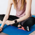 Bracelet Apple Watch EzStrap en silicone rigide à finition pailletée, style sport, porté au poignet d’une femme assise en tenue de sport sur un tapis de yoga bleu.