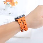 Bracelet Apple Watch EzStrap en silicone mat orange, de style sport avec une structure chaînée flexible, porté au poignet d’une personne devant un livre ouvert.