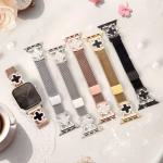 Bracelet Apple Watch EzStrap en métal milanais doré, style luxe avec motif trèfle incrusté de cristaux, présenté à plat sur une table décorative avec perles, fleurs et tasse de café.
