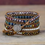 Bracelet Apple Watch EzStrap multi-couches en cuir tressé avec perles colorées et bouton gravé en métal, présenté en gros plan sur une surface en bois.