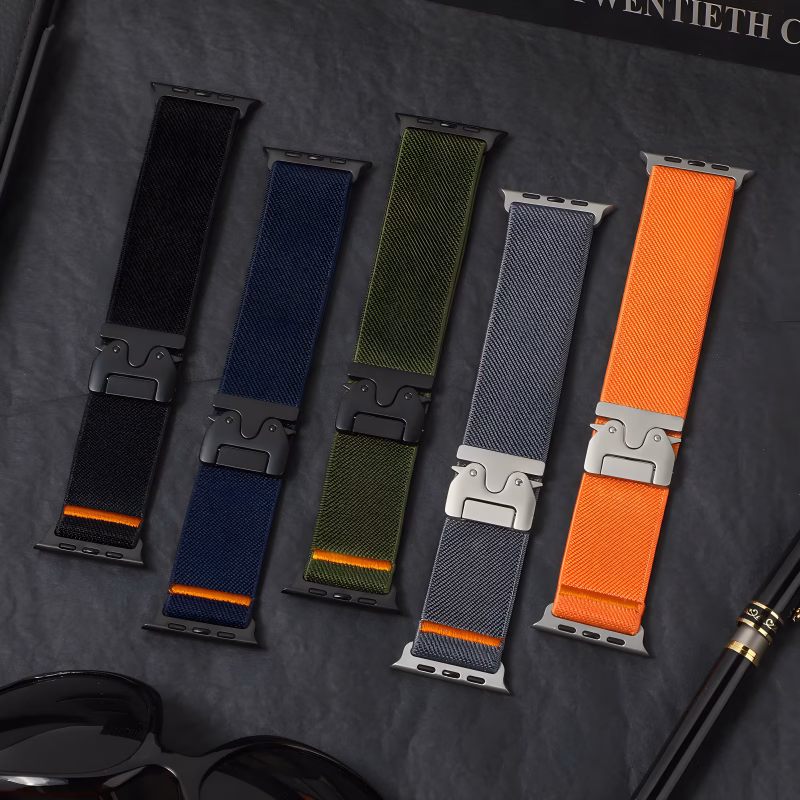 Bracelet Apple Watch EzStrap en nylon texturé de style sport, décliné en plusieurs coloris, posé sur une surface noire avec des accessoires autour.